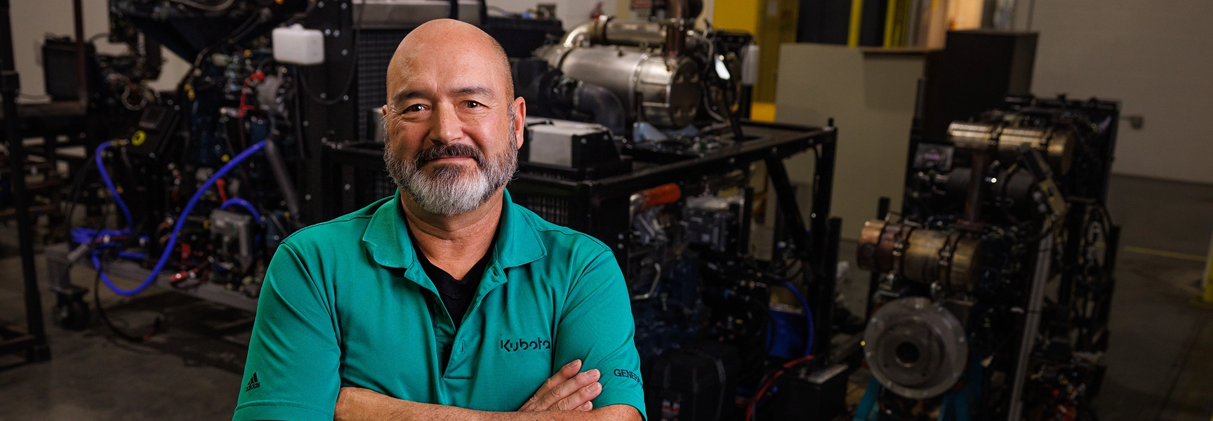 Kubota technician standing confidently in front of industrial engines in a service facility.